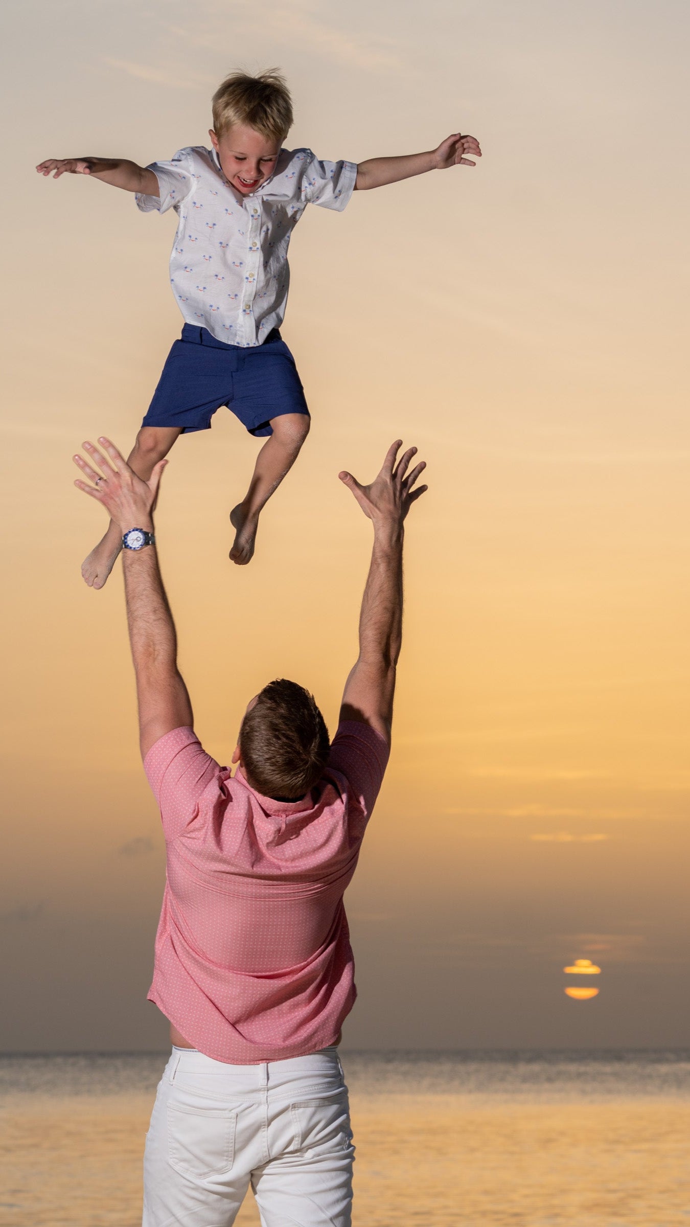 Man throwing a child into the air against a sunset sky Cayman Islands
