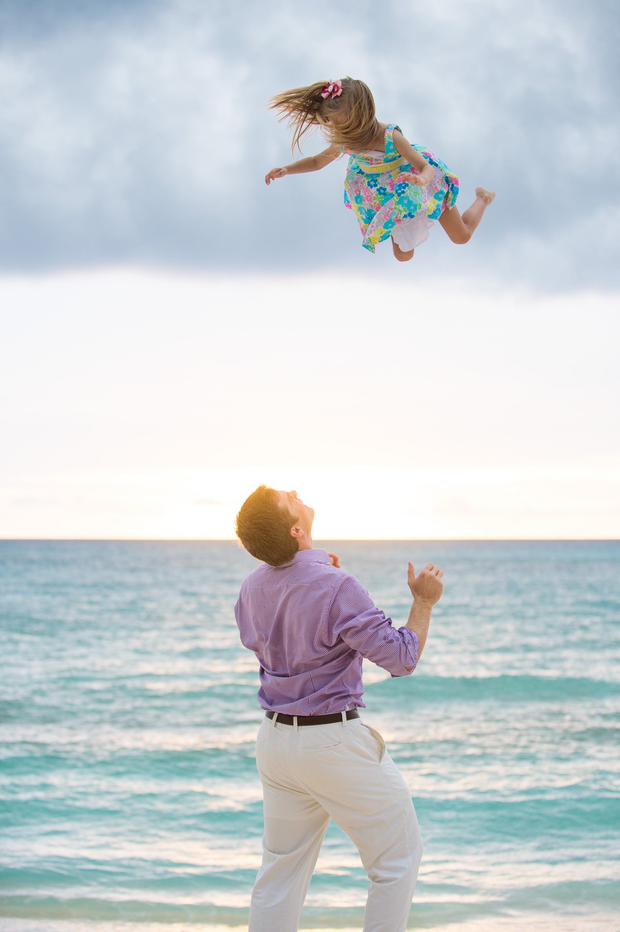 Man throwing a young girl into the air at the beach. Family portraits grand cayman