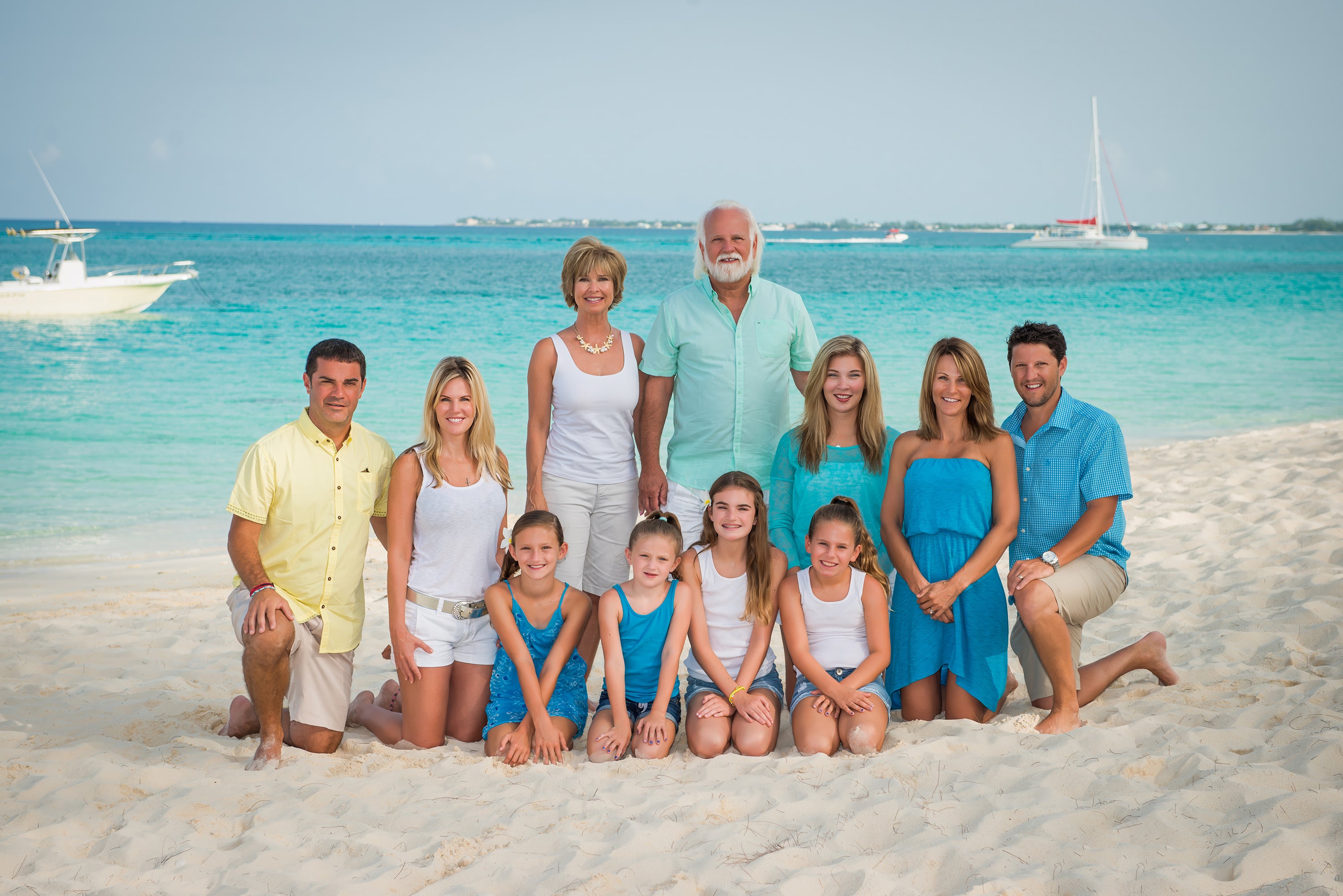 Family posing on a beach with clear blue water and boats in the background. Ritz-Carlton Grand Cayman family portrait photography.