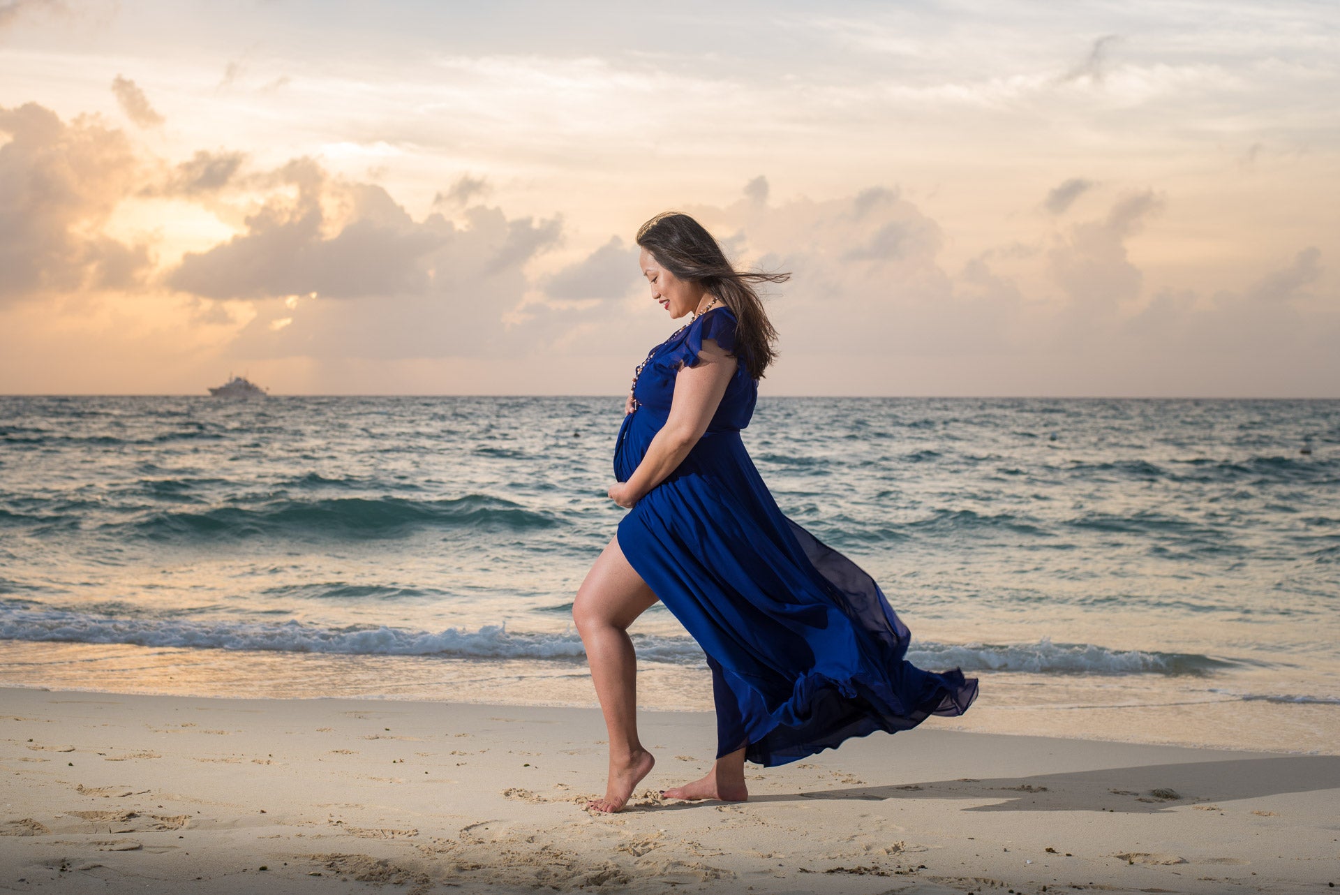 Woman in a blue dress standing on a beach at sunset during a pregnancy photo shoot at the Ritz-Carlton Grand Cayman