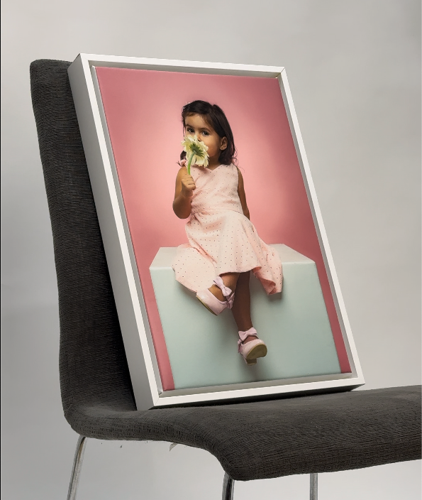 Framed photograph of a young girl holding flowers on a chair with a pink background. Printing, framing services Cayman Islands.