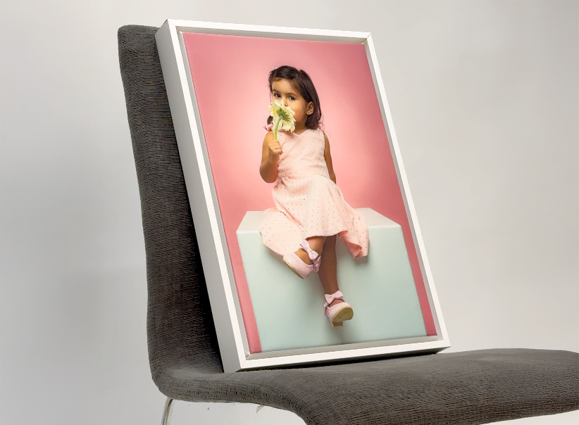Framed picture of a young girl holding a flower on a gray chair. Printing, framing services Cayman Islands.