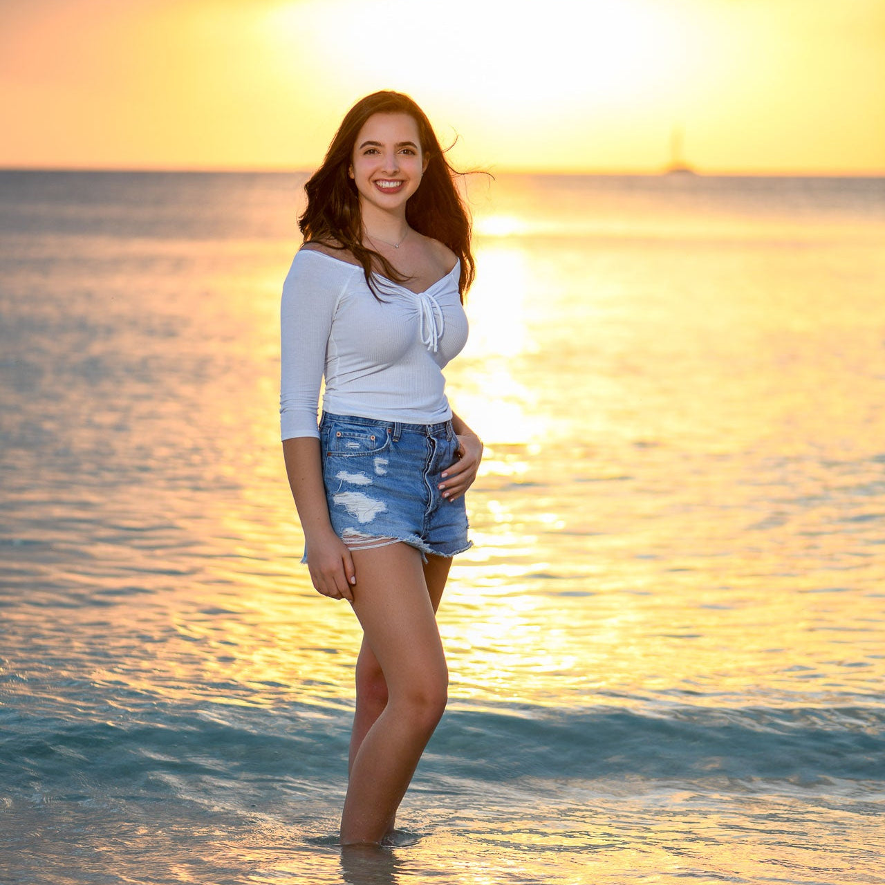 Woman standing in shallow water at sunset on a beach. Ritz-Carlton Grand Cayman. Senior portrait photography.