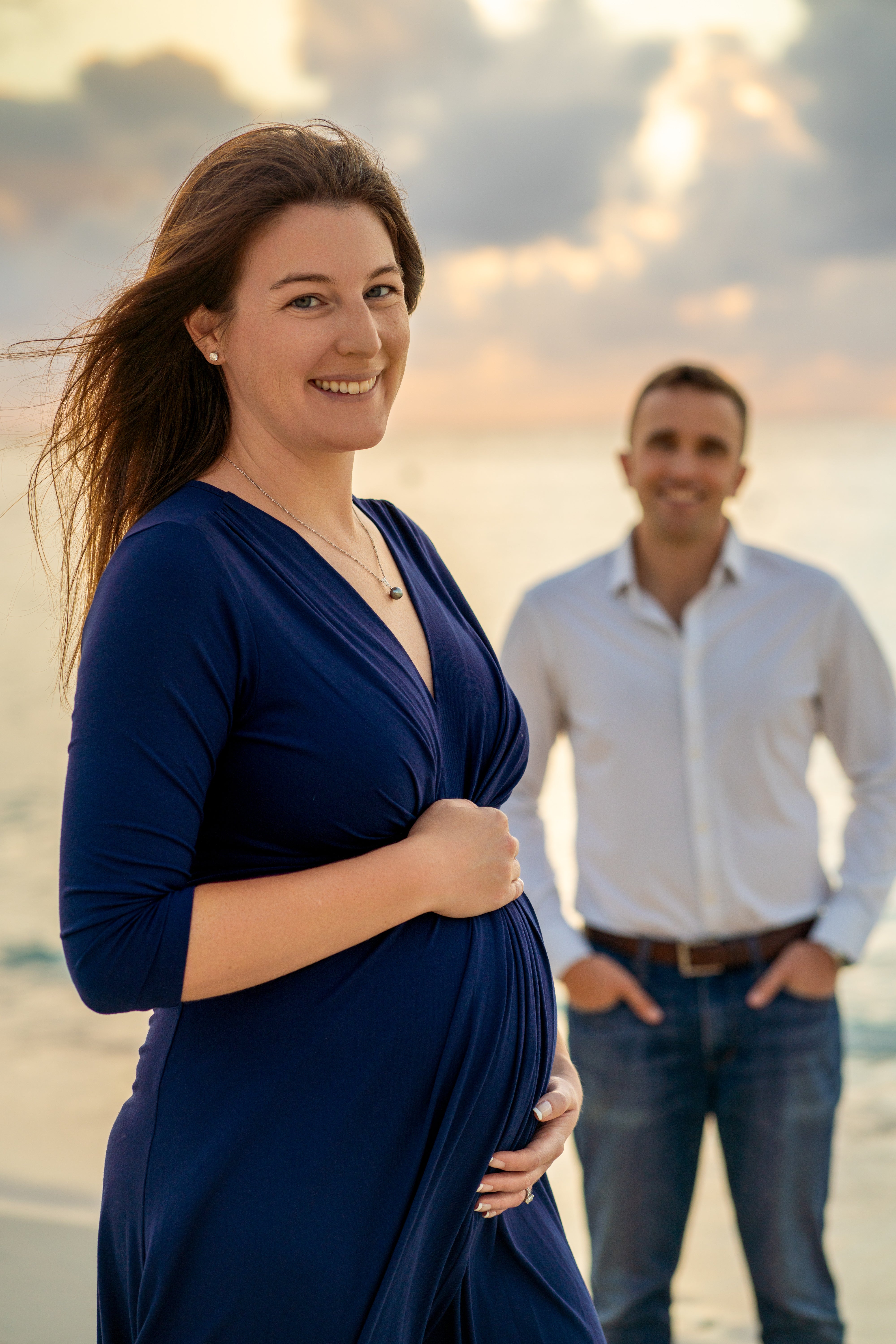 Pregnant woman in a blue dress standing on a beach during a cayman islands maternity shoot