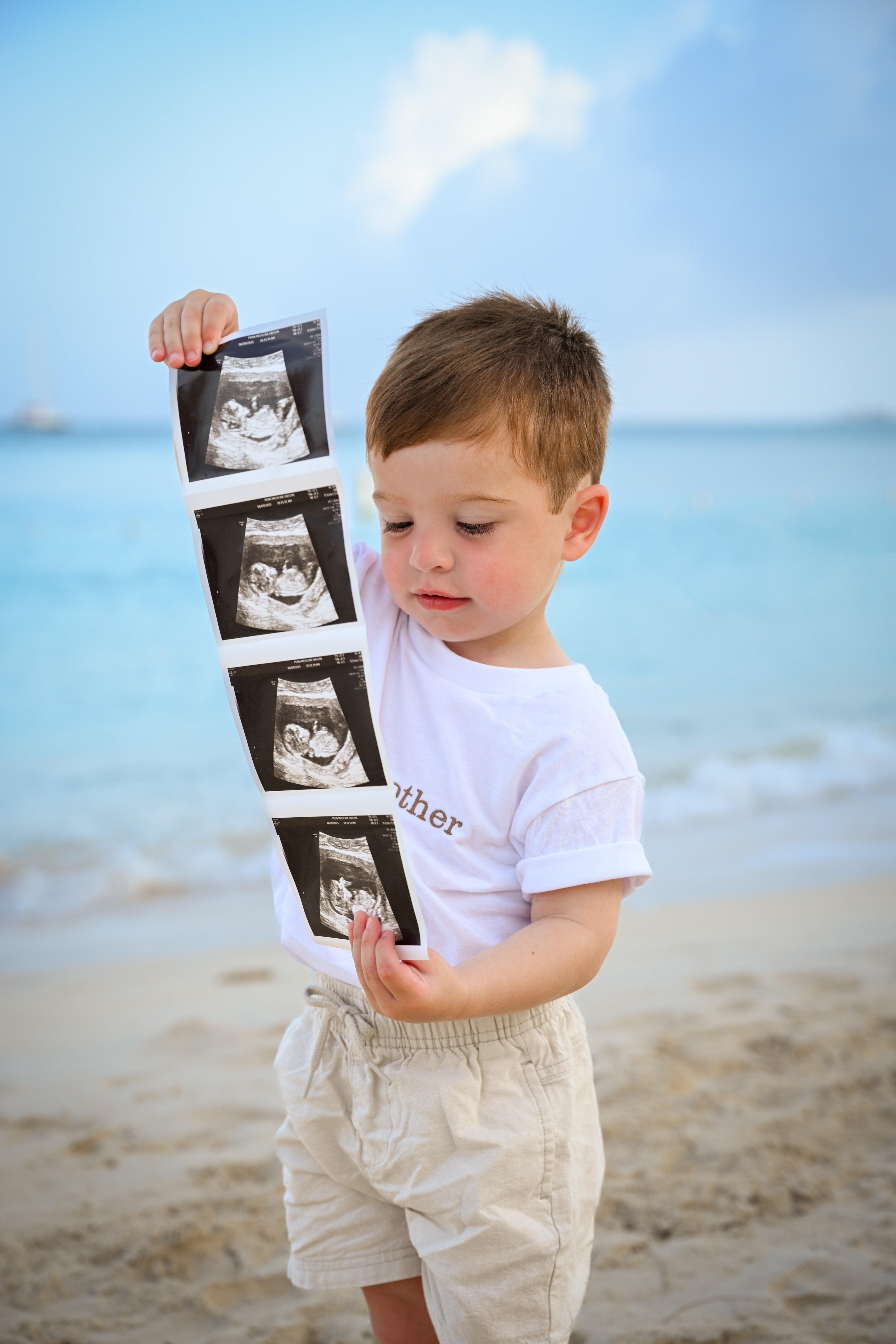 Child holding ultrasound images on a beach during a maternity shoot cayman islands